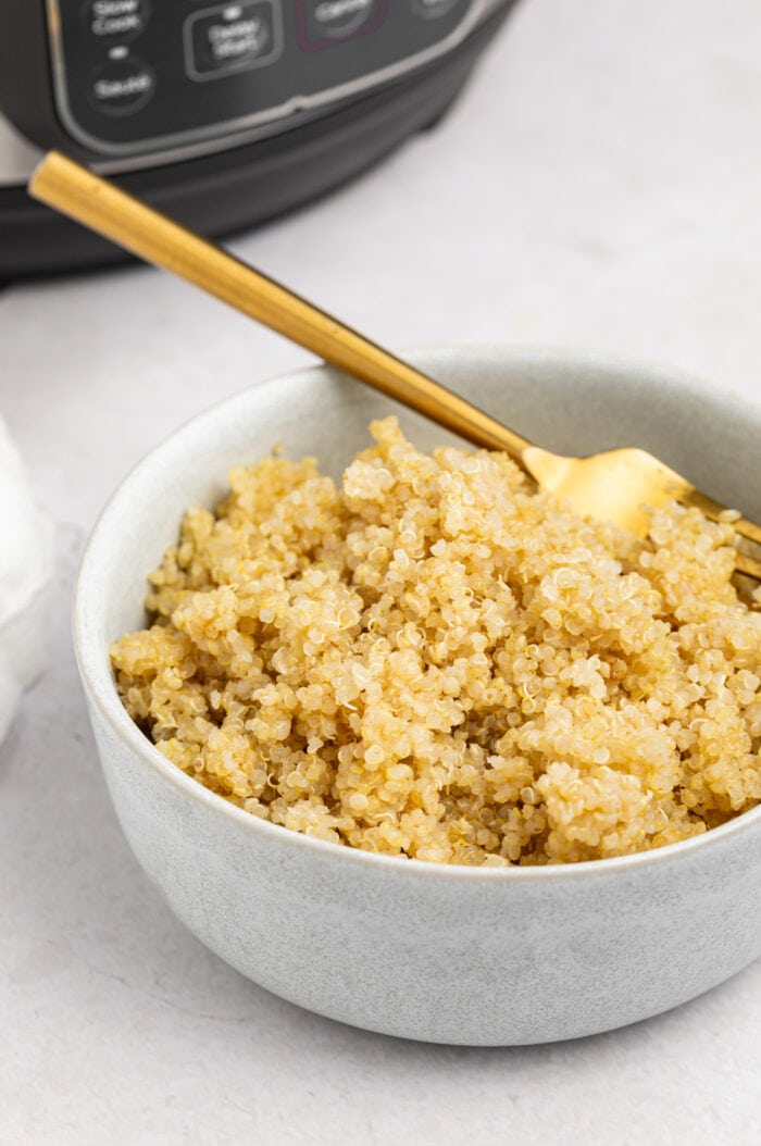 instant pot quinoa in a bowl with a fork and the instant pot on the table in the backgroud