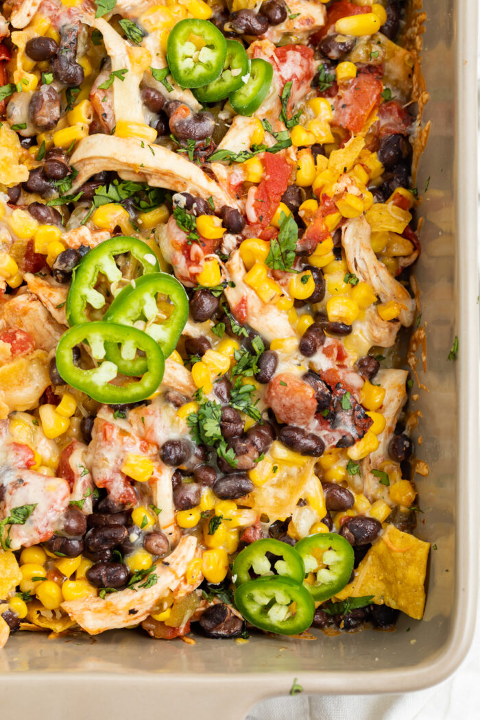 Overhead view of Mexican chicken casserole with tortilla chips, chicken, black beans, and corn, topped with cheese and jalapenos.