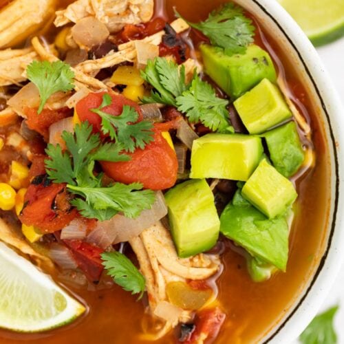 overhead image of mexican soup in a bowl with avocado, cilantro, and a lime wedge on top