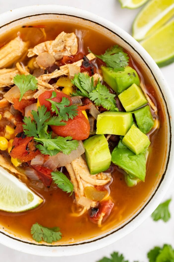 overhead image of mexican soup in a bowl with avocado, cilantro, and a lime wedge on top