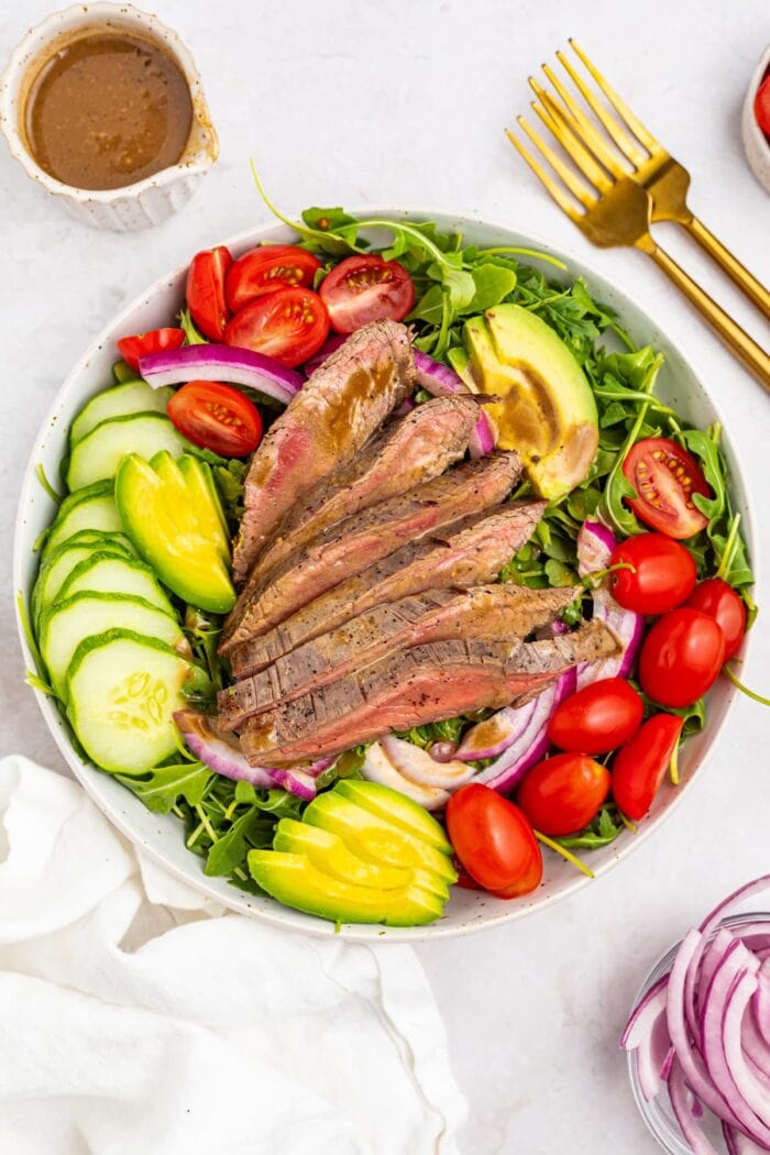 overhead image of steak salad with dressing, forks, and red onion on the side