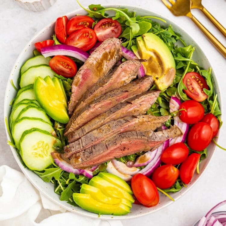 overhead image of steak salad with dressing, forks, and red onion on the side