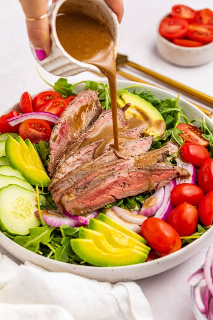 creamy balsamic dressing being poured over steak salad