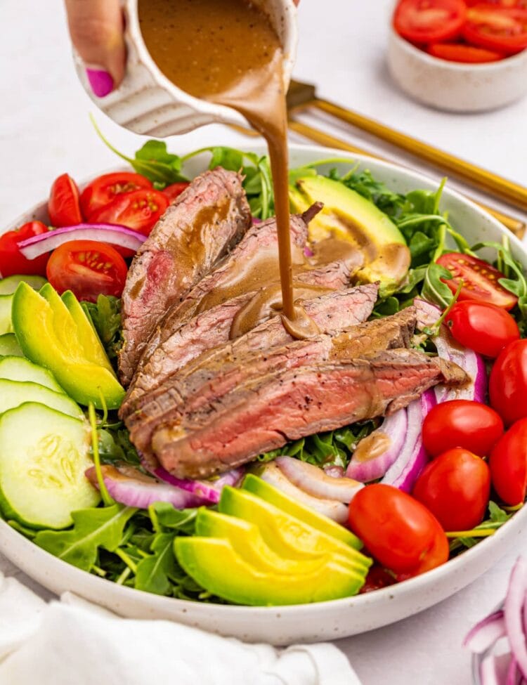 creamy balsamic dressing being poured over steak salad