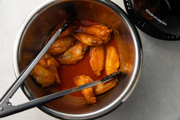 Air fryer chicken wings in large bowl with tongs