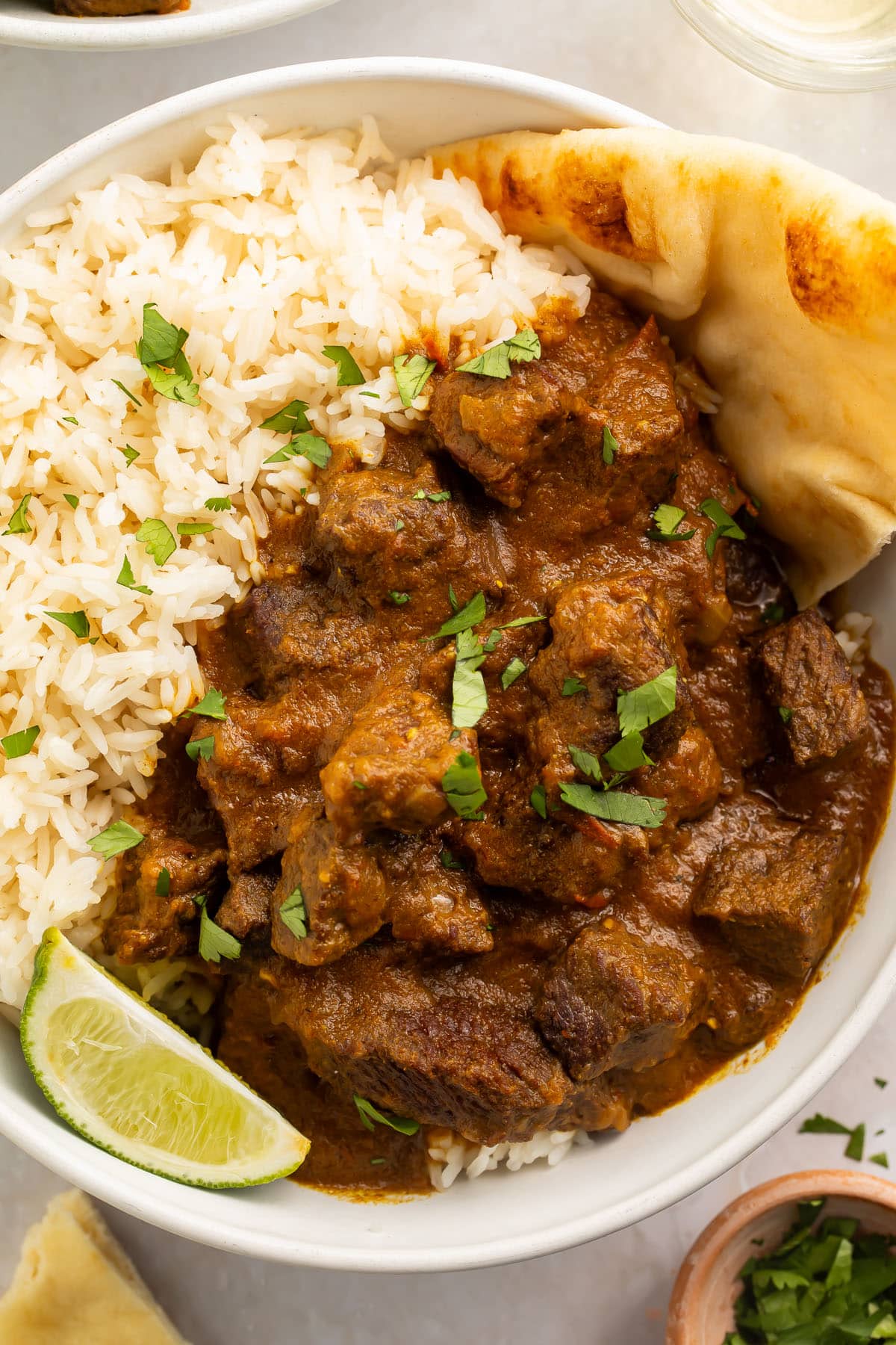 Close-up photo of beef curry with white rice in a bowl on a white background.