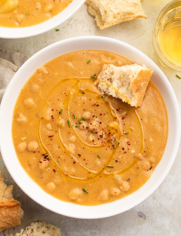 Top-down view of a white soup bowl holding creamy, golden chickpea soup with a piece of crusty bread resting in the soup.