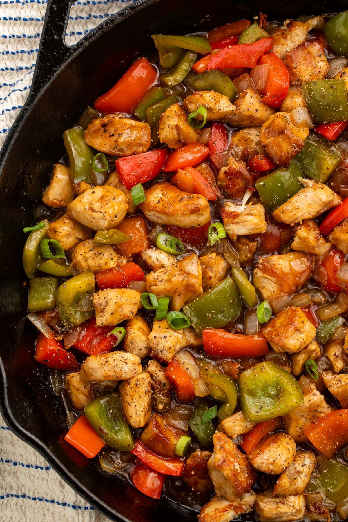 A large cast-iron skillet holding black pepper chicken and vegetables.