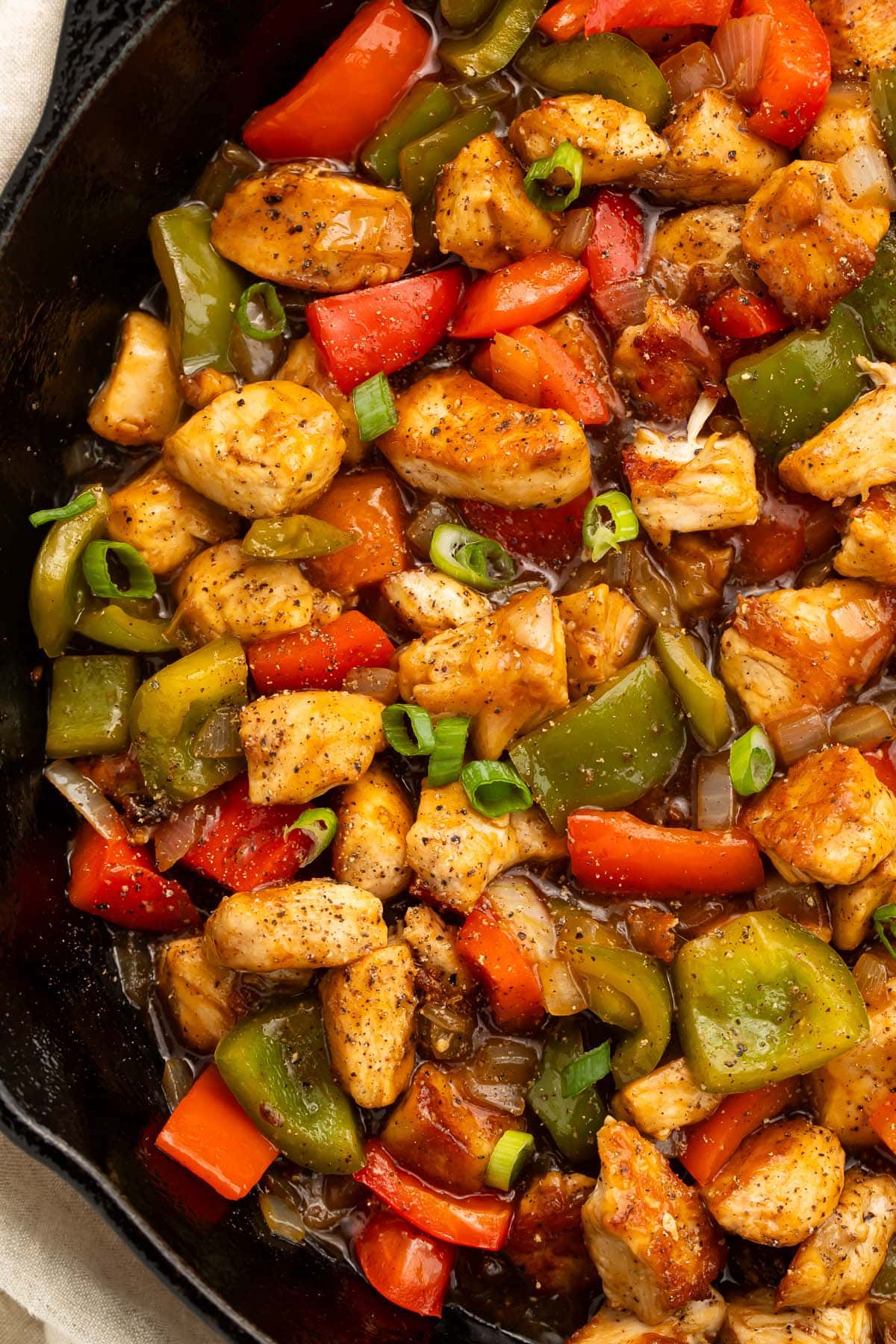 A large cast-iron skillet holding black pepper chicken and vegetables.