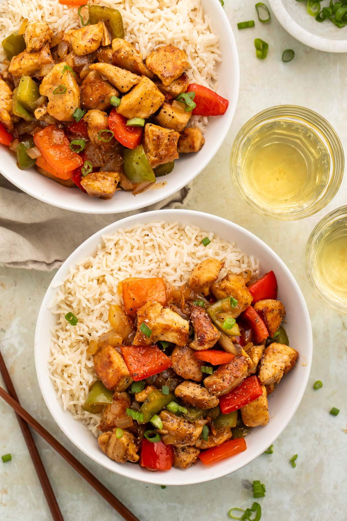 Overhead photo of a bowl of white rice topped with black pepper chicken and vegetables on a table.