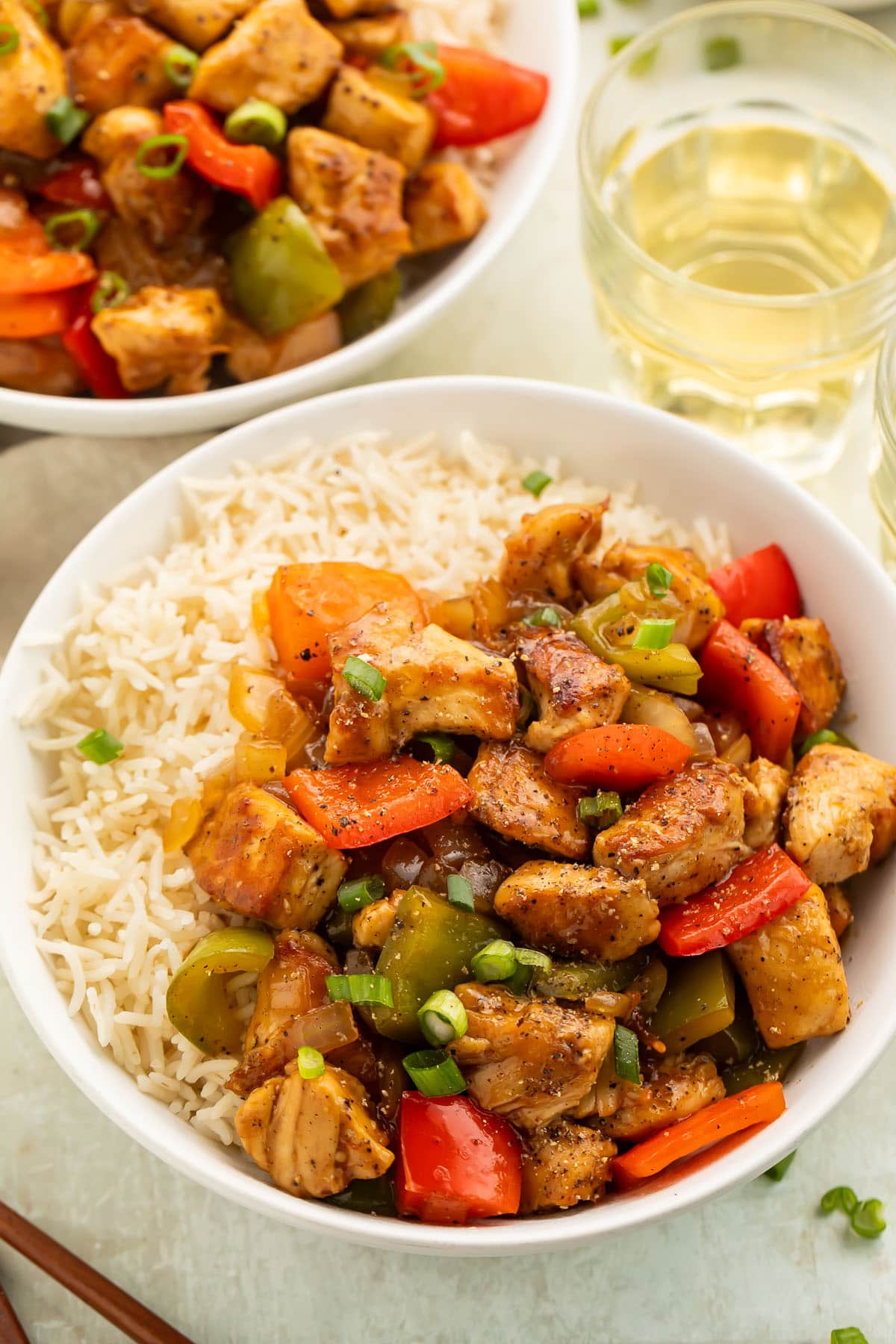 Close-up photo of a bowl of white rice topped with black pepper chicken and vegetables on a table.