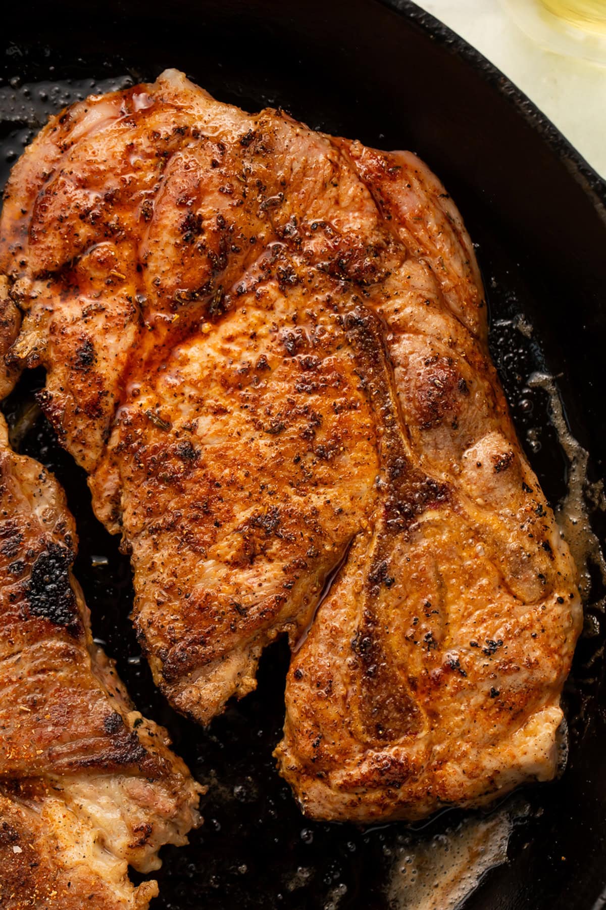 A juicy, pan-seared pork chop, seasoned with pork chop seasoning, in a cast iron skillet.