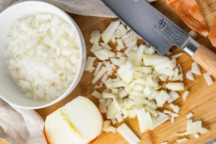 Diced onion on a cutting board next to a bowl of diced onion and a sharp knife
