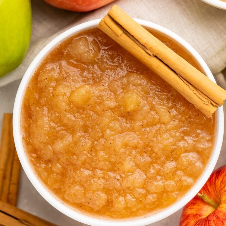Instant Pot applesauce in a large bowl surrounded by apples and topped with a whole cinnamon stick