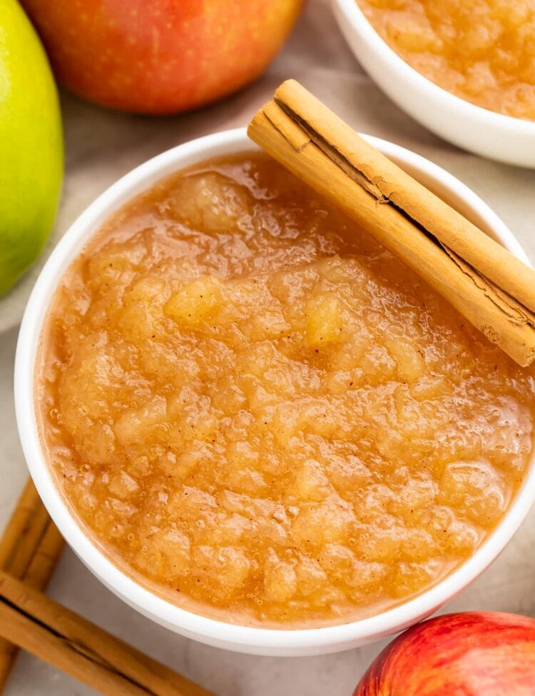 Instant Pot applesauce in a large bowl surrounded by apples and topped with a whole cinnamon stick