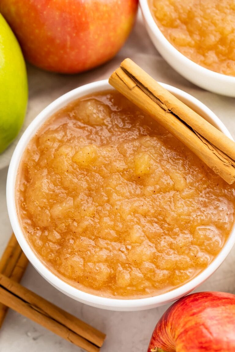 Instant Pot applesauce in a large bowl surrounded by apples and topped with a whole cinnamon stick