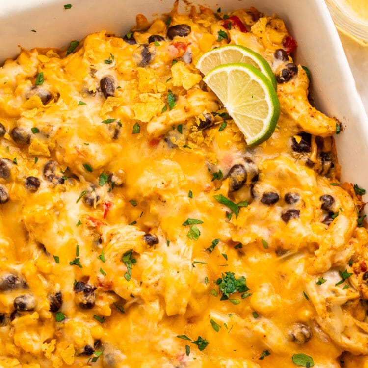 Overhead view of a casserole dish holding a Mexican chicken casserole topped with melted cheese and two lime wedges.
