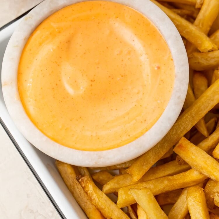 A small bowl of sriracha mayo on a baking sheet with fries