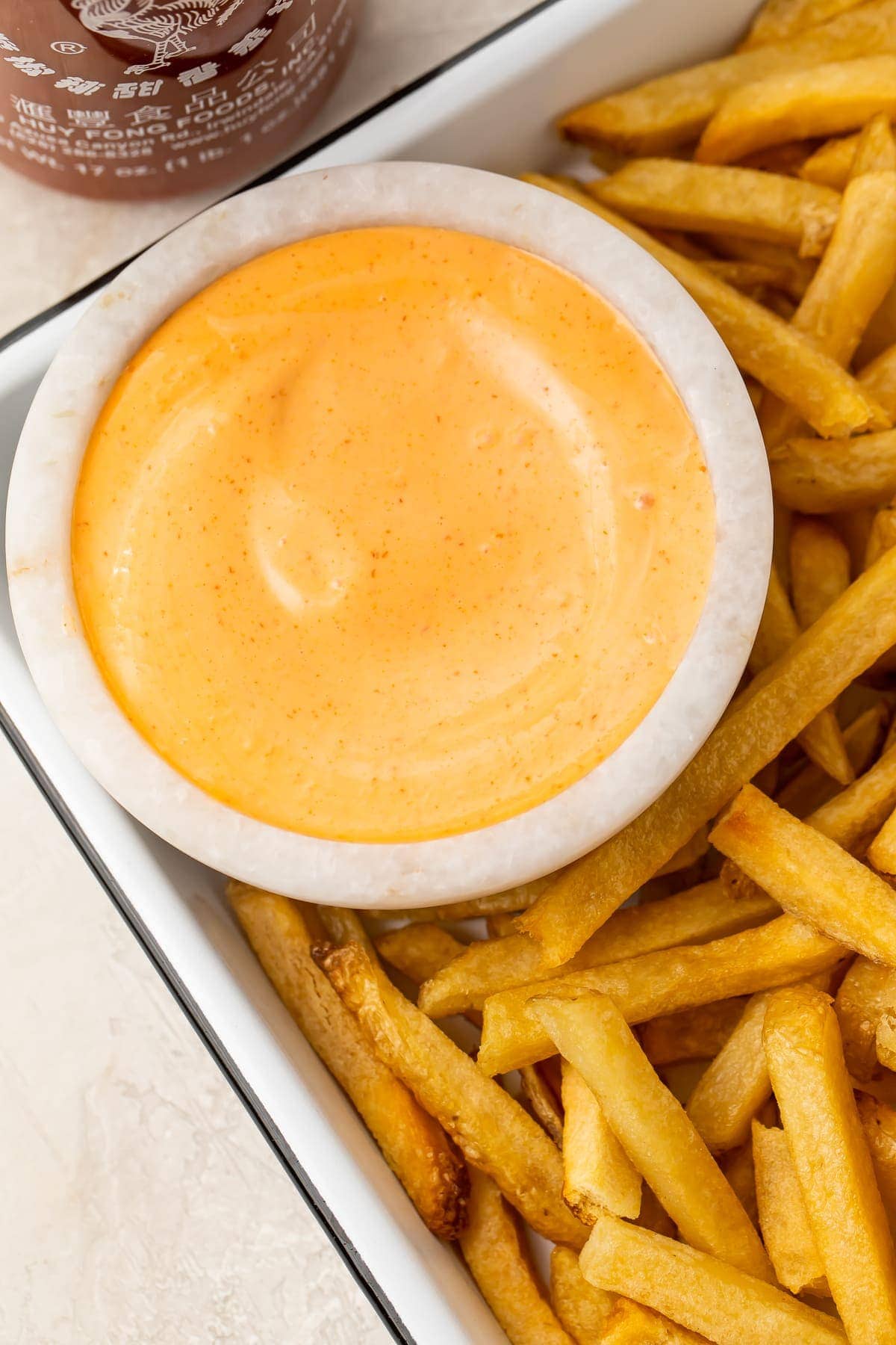 A small bowl of sriracha mayo on a baking sheet with fries