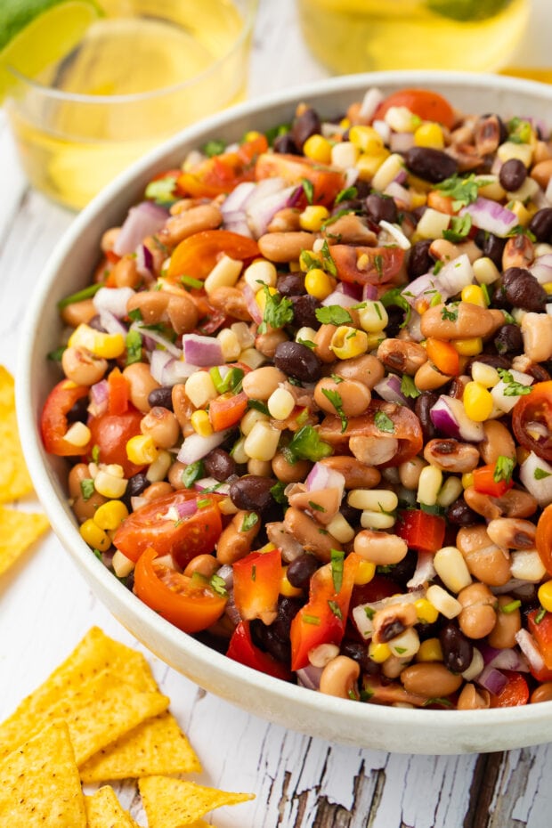Texas caviar in a white bowl surrounded by yellow corn tortilla chips.