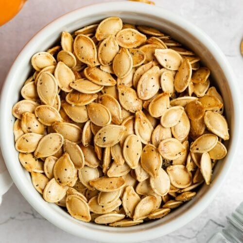 air fryer pumpkin seeds in a dish with a pumpkin on the side