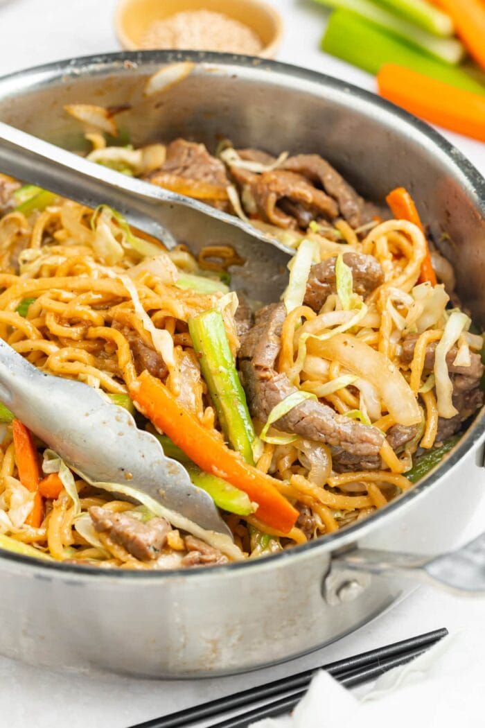 beef chow mein in a skillet with tongs