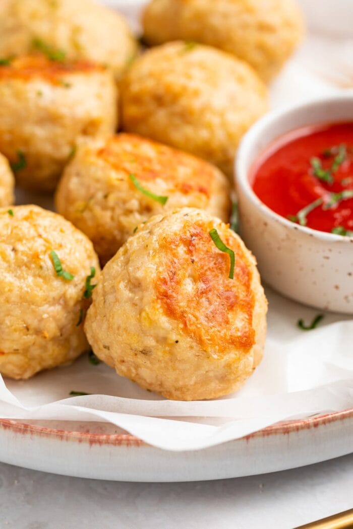 close-up image of baked chicken meatballs on a plate with tomato sauce on the side