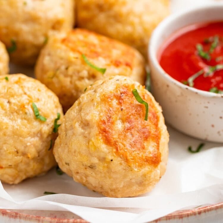 close-up image of baked chicken meatballs on a plate with tomato sauce on the side