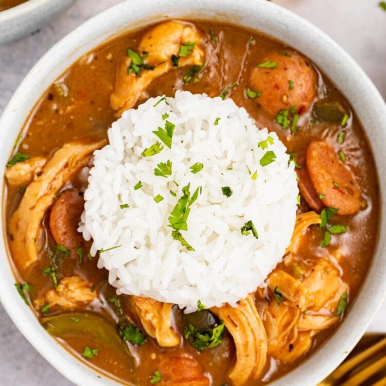 chicken and sausage gumbo in a bowl with a scoop or rice on top