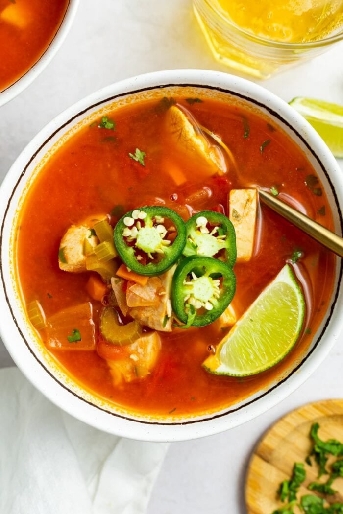 overhead image of a bowl of mexican chicken soup with sliced jalapenos and a lime wedge on top