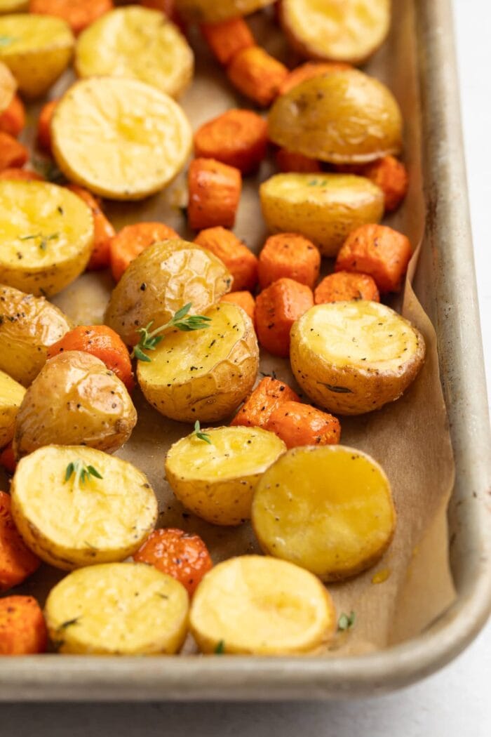 roasted potatoes and carrots on a baking sheet with fresh thyme on top