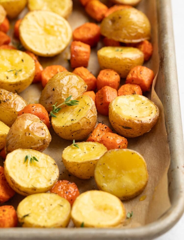 roasted potatoes and carrots on a baking sheet with fresh thyme on top