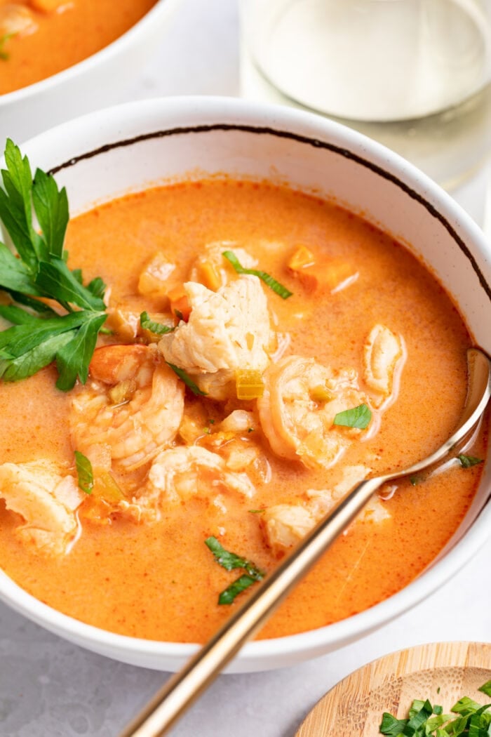 seafood soup in a bowl with a spoon with white wine and fresh parsley on the side