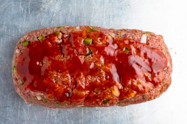 Uncooked meatloaf with glaze on baking sheet