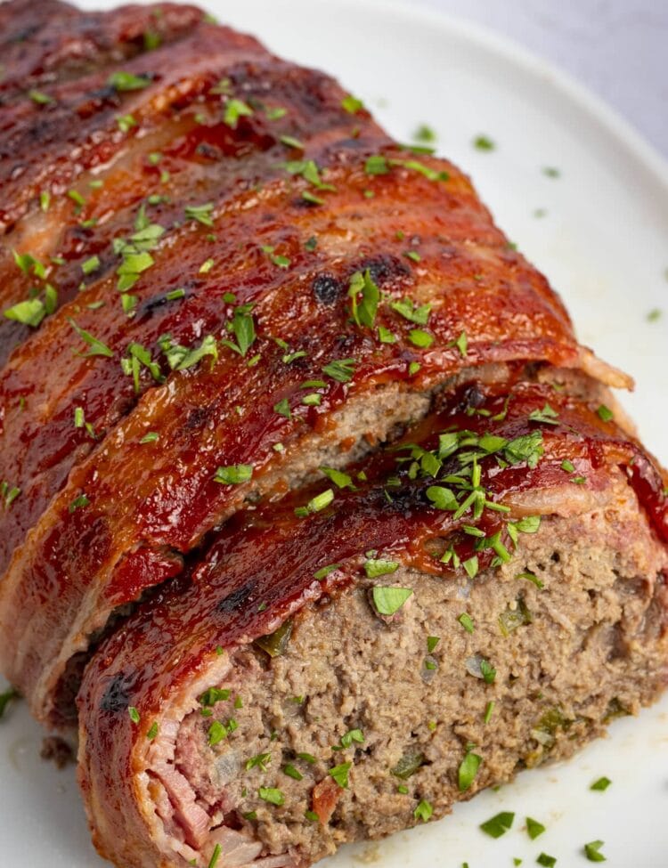 Overhead view of bacon wrapped meatloaf with ketchup and garnish on a white plate
