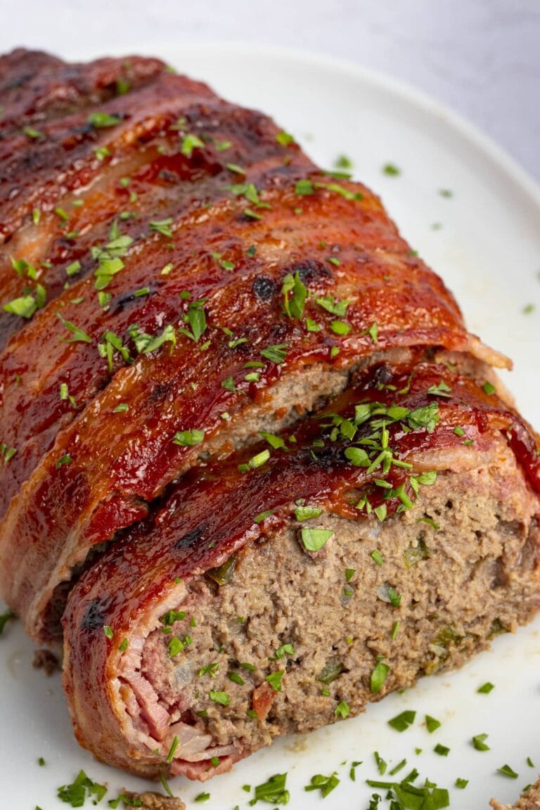 Overhead view of bacon wrapped meatloaf with ketchup and garnish on a white plate