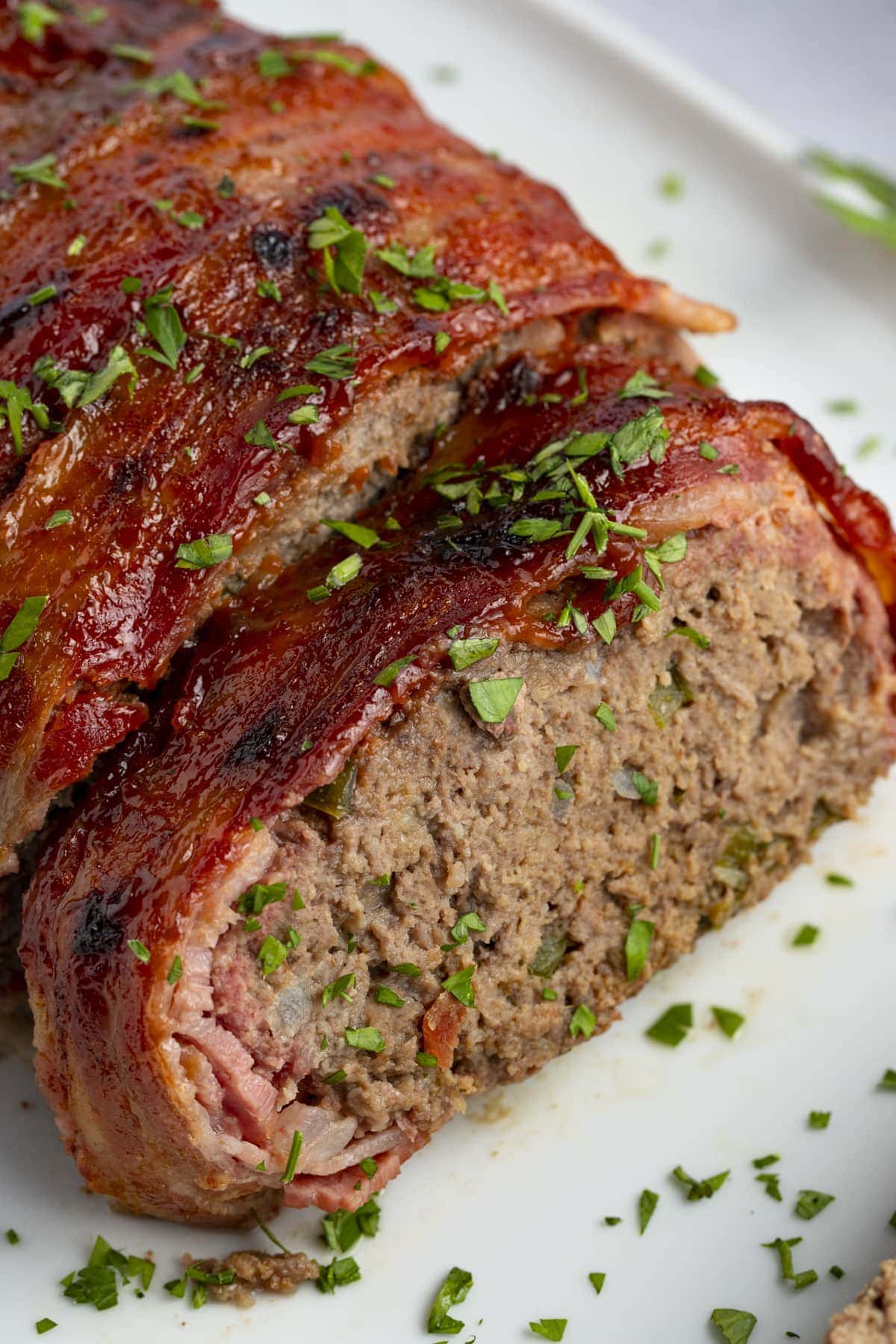 Bacon wrapped meatloaf slices on a white plate with ketchup and garnish