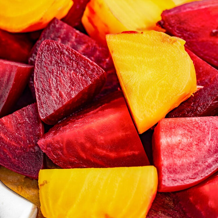 Large chunks of red and yellow beets on a wooden cutting board.