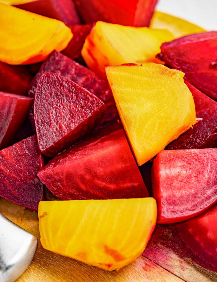 Large chunks of red and yellow beets on a wooden cutting board.