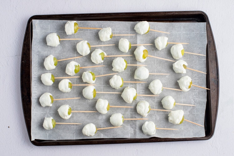 Yogurt-covered grapes with toothpicks lined up on a baking sheet lined with parchment paper