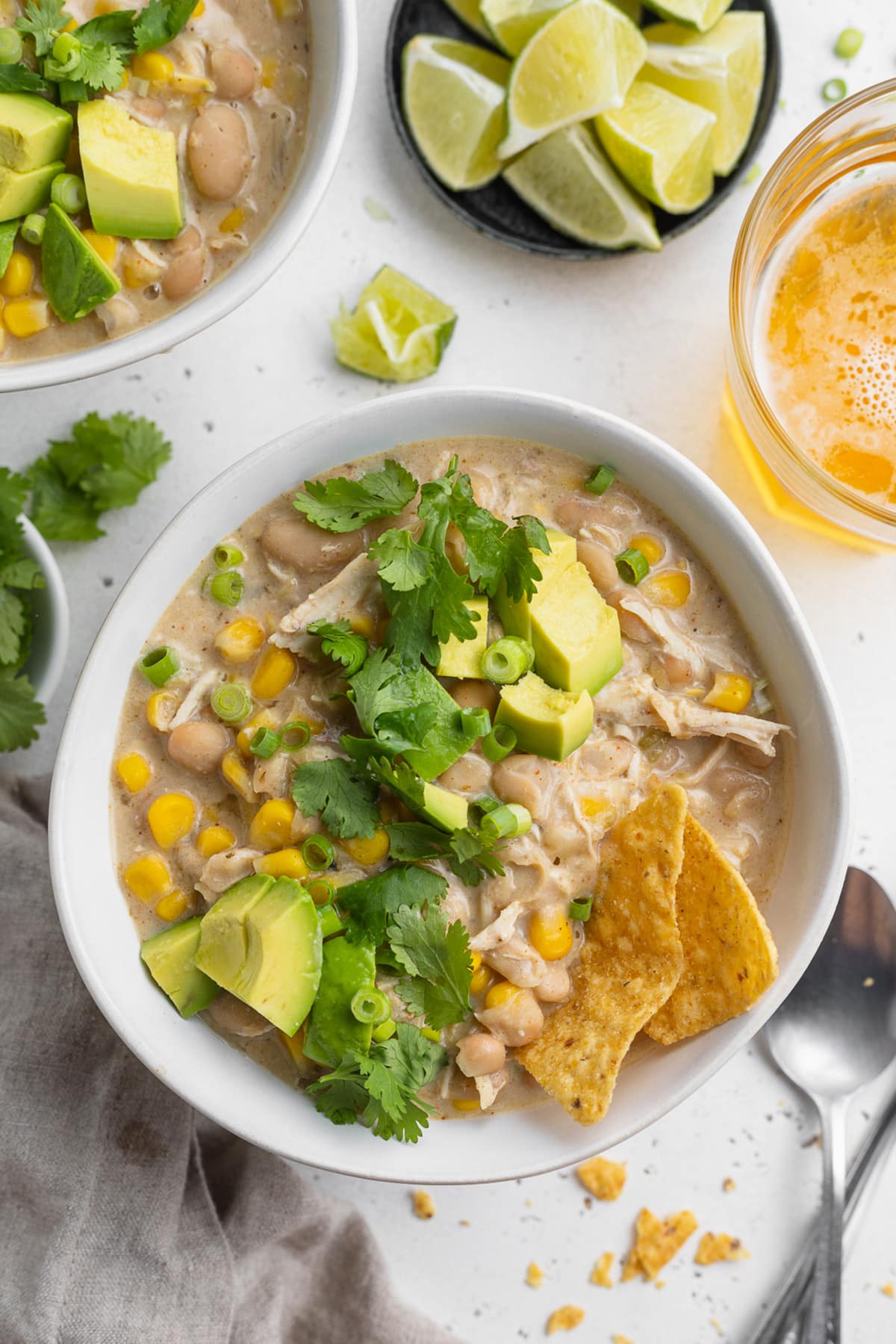 Top-down view of a bowl of Instant Pot white chicken chili on a neutral tabletop with a glass of white wine and a bowl of lime wedges.