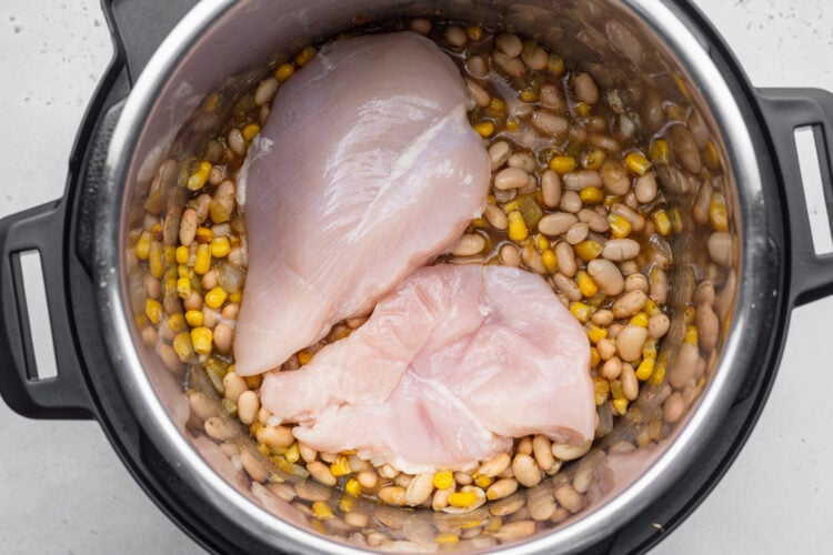 Uncooked chicken on top of a bed of ingredients for white chicken chili in the Instant Pot.