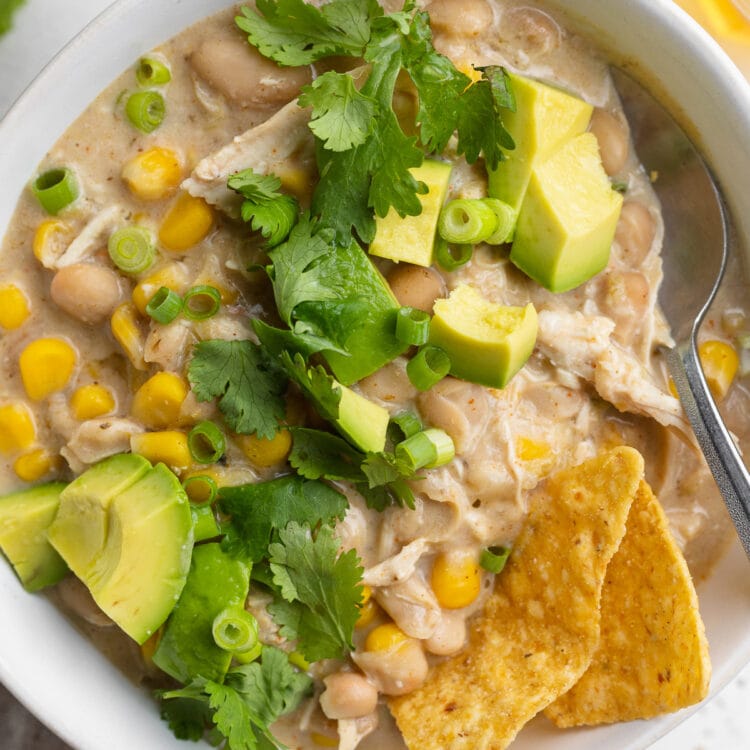 Overhead view of a bowl of white chicken chili, cooked in the Instant Pot, with avocado, cilantro, and tortilla chips.