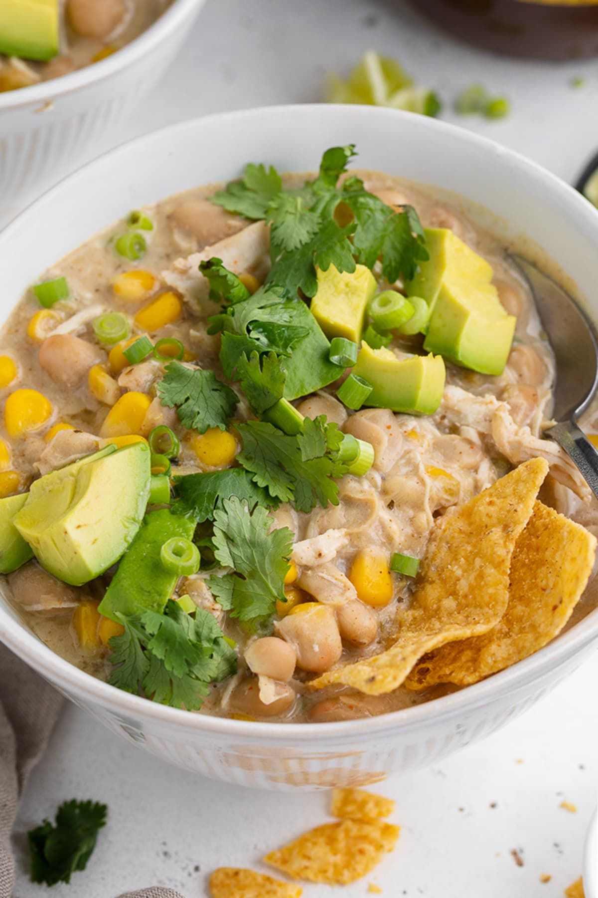 Angled view of a bowl of Instant Pot white chicken chili topped with avocado, cilantro, and tortilla chips.