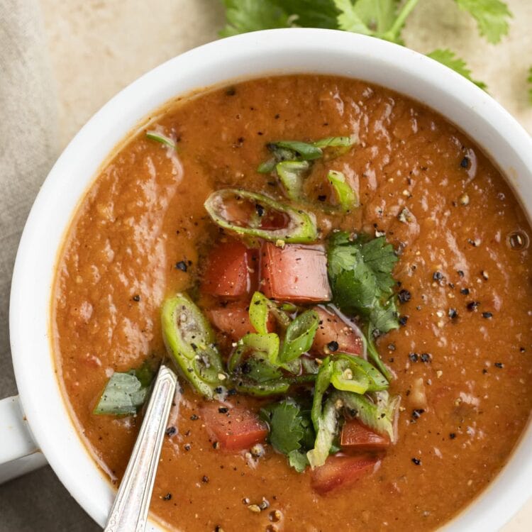 A large cup of pinto bean soup topped with cilantro, lime, tomatoes, and green onions