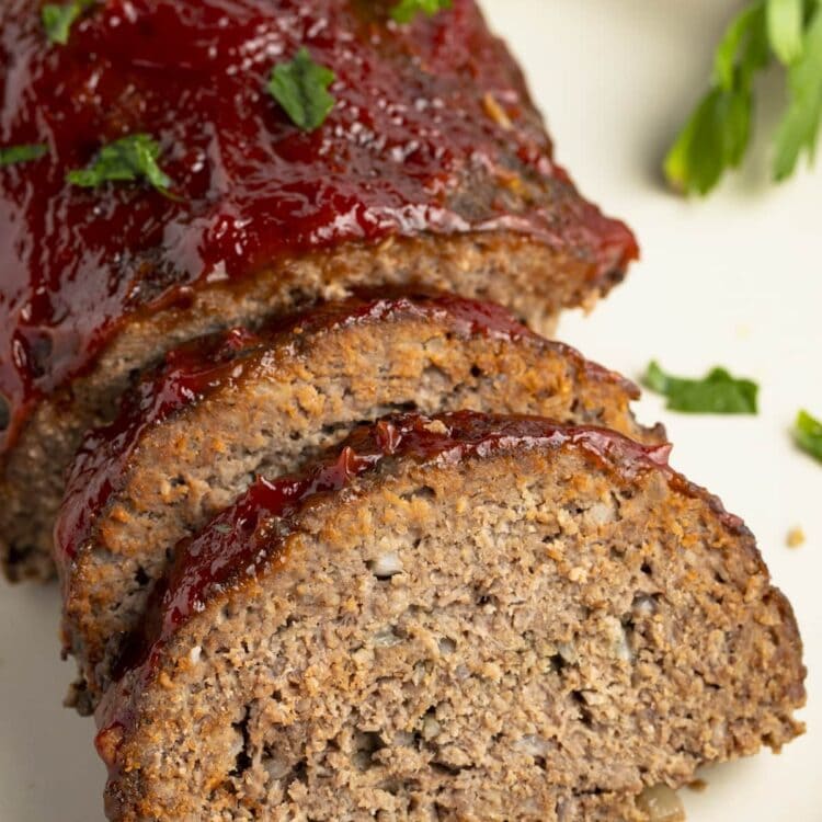 Slow cooker meatloaf, photographed from an overhead angle, with two slices leaning up against the end of the loaf on a white plate