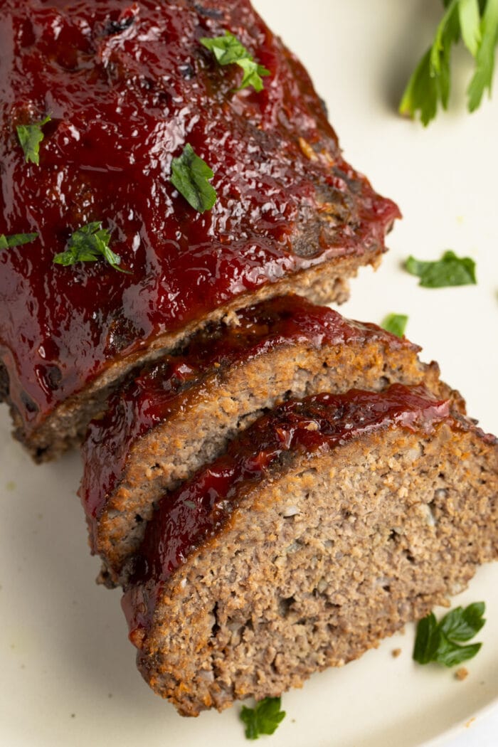 Slow cooker meatloaf, photographed from an overhead angle, with two slices leaning up against the end of the loaf on a white plate