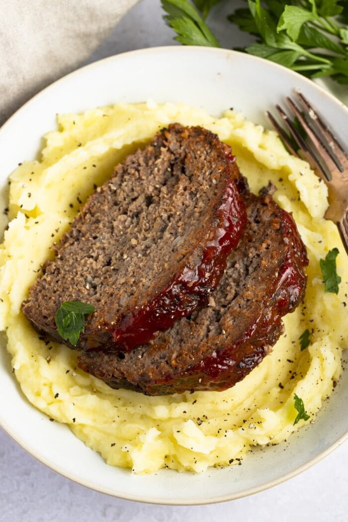 2 pieces of slow cooker meatloaf on a bed of mashed potatoes