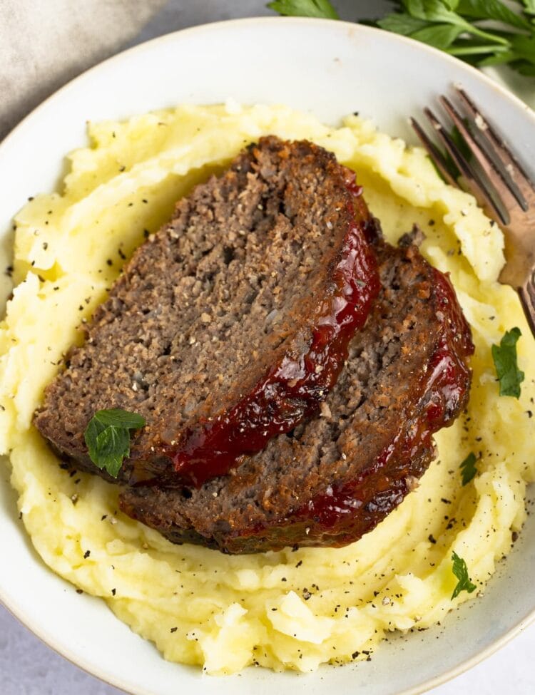2 pieces of slow cooker meatloaf on a bed of mashed potatoes