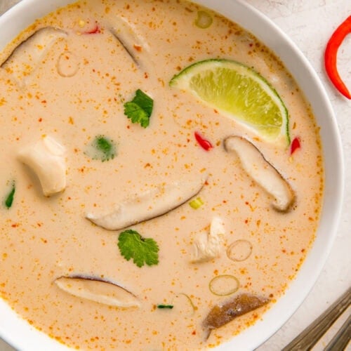 Crockpot Tom Kha Gai soup in a white bowl on a table next to lime wedges.